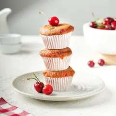 A playful stack of three cherry-topped muffins. The bright, clean background and simple styling make this a classic and appealing shot for any bakery.