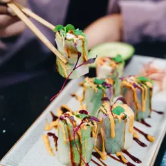 A vibrant shot of summer rolls being picked up with chopsticks. The focus is on the fresh ingredients and the colorful sauces, making it look like a light and delicious appetizer.
