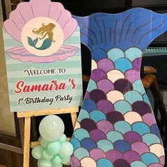 A personalized welcome sign for a mermaid-themed first birthday party. This custom easel stand features a mermaid in a clamshell and is paired with a large mermaid tail cutout, setting the theme right from the entrance.