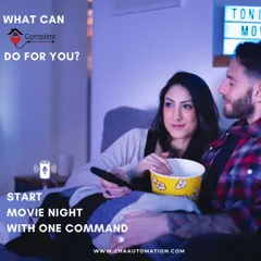 This is the result of our work: effortless enjoyment. A couple relaxes for a movie night, having used a single command to dim the lights and start the film, demonstrating the convenience of a smart living room.