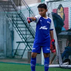 A young goalkeeper stands ready and focused in front of the goal. We provide specialized training for all positions, ensuring every player develops the specific skills they need.