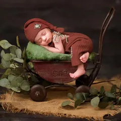 This baby is posed in a miniature vintage-style cart, surrounded by eucalyptus leaves on a burlap surface, showcasing our detailed rustic setups.