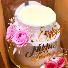 This two-tier engagement cake features a white chocolate drip, fresh pink roses, and custom gold acrylic name toppers for the happy couple.