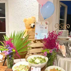 An adorable baby shower setup with a teddy bear theme. The buffet includes a variety of fresh salads and other dishes, all decorated with pink and blue balloons to match the occasion.