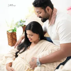A tender moment between a couple in a cozy, boho-themed setup. The earthy tones and soft fabrics create a warm and intimate environment for their maternity shoot.
