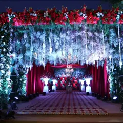 A grand and dramatic entrance for a reception. The walkway is defined by a ceiling of hanging white and blue flowers, framed by lush greenery and rich red draping for a luxurious feel.