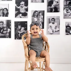 A beautiful first birthday portrait. This little girl is all smiles, sitting in a miniature wicker chair against a backdrop of her own baby photos.