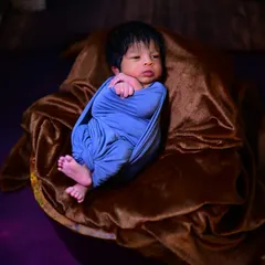 A simple and sweet newborn photo. The baby is comfortably swaddled in a blue wrap, resting on a soft brown blanket, highlighting their delicate features.