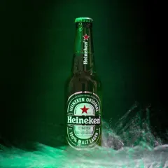 A commercial shot of a Heineken bottle with a dynamic water splash against a signature green background, showcasing skills in beverage advertising photography.