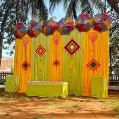 A bright and sunny outdoor setup for a Haldi or Mehendi function. The yellow drapes are decorated with colorful Rajasthani umbrellas and hangings, perfect for a daytime event.