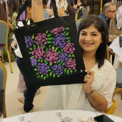 A guest at a baby shower proudly holds up the beautiful floral tote bag she painted for the mom-to-be. This is a heartfelt way for friends and family to create personalized, useful gifts together.