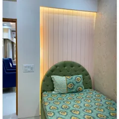 A cozy corner bedroom with a custom green upholstered headboard and backlit fluted paneling. This design is perfect for a smaller room, making it feel special and personalized.