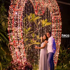 Framed by a giant heart made of countless fairy lights. This is a classic romantic shot that beautifully captures the couple's joy and the magical ambiance of the night.