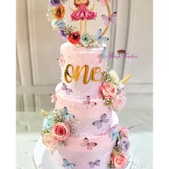 A sweet celebration for a magical 'one'-derland. This three-tier pink cake is decorated with butterflies, flowers, and a cute doll topper inside a floral wreath.