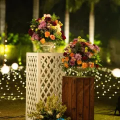 A nighttime shot of our floral pedestals, with arrangements of colorful flowers set against a backdrop of twinkling fairy lights. This combination of rustic wood, classic lattice, and warm light creates a magical garden feel.