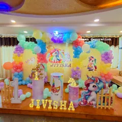 A magical unicorn-themed first birthday party. I used a pastel rainbow balloon arch, unicorn character cutouts, themed plinths, and the name 'Jivisha' in marquee letters.