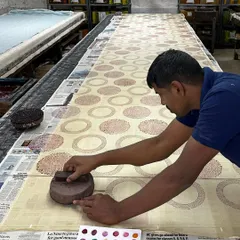 The steady hand of a master artisan at work. Here, one of our printers carefully aligns a teak block to create a seamless pattern on a long stretch of fabric, a skill honed over decades of practice.