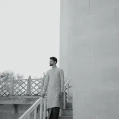 A stylish black and white portrait of the groom in his traditional attire. The architectural background and his confident pose create a modern yet timeless look.
