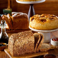 A beautiful spread of various freshly baked breads and cakes. This shot showcases the variety available at a bakery, from multigrain loaves to sweet focaccia, arranged to look like a generous, welcoming feast.