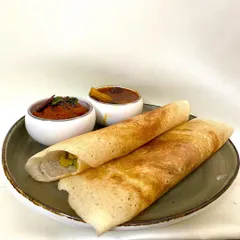A perfectly cooked Masala Dosa, golden and crisp, filled with spiced potatoes. It is served with a bowl of tangy sambar with drumsticks and a spicy red chutney.
