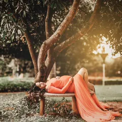 A serene outdoor maternity portrait. The flowing orange gown and natural setting are paired with soft, romantic makeup to create a truly beautiful and artistic memory.