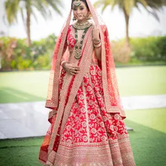 A full-length portrait of a bride looking absolutely majestic. The soft glam makeup with defined eyes stands out beautifully against her ornate red and gold lehenga, creating a truly royal vision.
