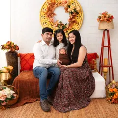 A complete family portrait featuring parents, an older daughter, and a newborn, all seated together in a warm, rustic-themed setup. We compose these shots to feel natural and full of love, creating a beautiful record of your family at this milestone.