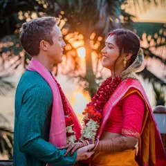 A beautiful sunset portrait of a couple on their wedding day. The warm, golden light of the setting sun creates a romantic backdrop, highlighting their traditional garments and happy expressions.