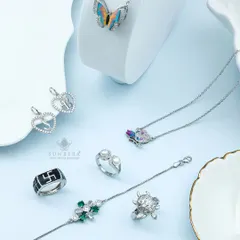 A statement in silver. This image displays a range of my custom silver pieces, including a butterfly pendant, initial heart charms, a men's Swastik ring, and a delicate bracelet with green gemstones.
