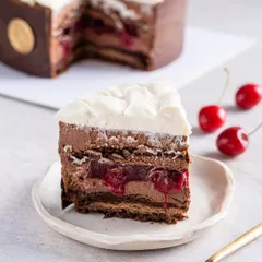 A perfect slice of our modern Black Forest Entremet, revealing layers of rich chocolate mousse, tangy cherry confit, and light whipped cream. This is a sophisticated reinterpretation of a classic, showcasing our dedication to flavour and texture.