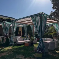 An elegant outdoor lounge created for a Tennis Club party. The custom-built canopy with striped green and white curtains provides shade and defines a sophisticated seating area for guests.