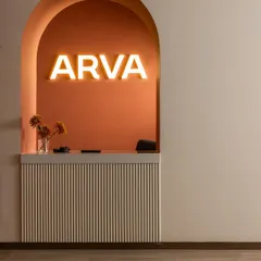 The arched reception desk at ARVA Clinic, a design element with a story. Inspired by the idea of a London phone booth turned inside out, it transforms a symbol of private calls into a welcoming space for open conversation, highlighted by the warm glow of the brand's name.