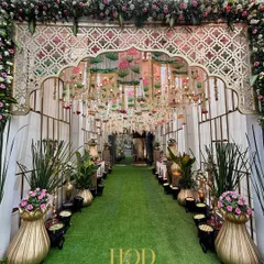 Your guests' first "wow" moment starts here. I love creating immersive entrances like this one, with a lush green carpet, grand floral arches, and a ceiling of hanging chandeliers and lotus-themed drapes to build anticipation for the celebration ahead.