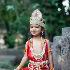 A close-up shot capturing the gentle smile of a boy in a detailed Krishna costume during an outdoor photoshoot.