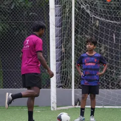 A coach demonstrates the proper way to strike a ball while a young player observes intently. This direct mentorship is a core part of our 1-on-1 coaching.
