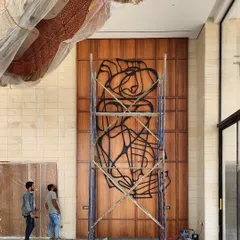 This image captures the installation process of a large-scale abstract line art piece on a towering wooden wall. It demonstrates our approach to integrating bold metal sculptures into architectural surfaces, creating a focal point that is both raw and refined.