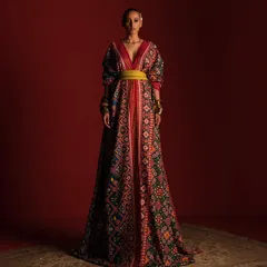 A full-length view of the Ravissant Patola-style kaftan. This shot showcases the magnificent drape and length of the garment, styled to create a regal and imposing silhouette against a deep red background.