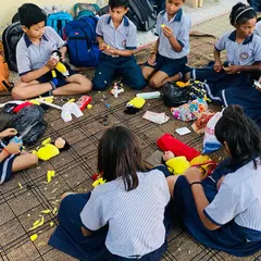School children sitting on the floor, completely focused on making their own puppets. My workshops for kids use simple materials so everyone can join in and have fun.