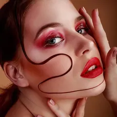 Combining bold color with textural details. This look features a bright red eyeshadow, a matching lip, and a graphic swirl applied to the face for an artistic, avant-garde effect.