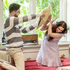 A fun and energetic pillow fight on the bed. This shot is full of laughter and action, perfectly capturing the couple's playful and carefree dynamic in a cozy indoor setting.