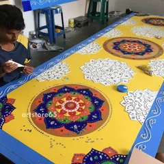 An artist works on a large panel featuring multiple mandala designs. This piece, created for a showroom, combines bright yellow and blue for a striking effect, showing how we adapt traditional designs for modern spaces.
