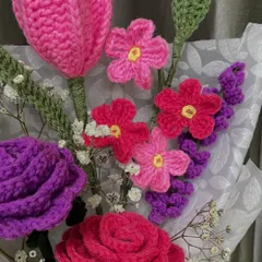 A closer look at the vibrant colors in this handmade bouquet. You can see the detailed stitch work in the purple rose, the pink tulip, and the smaller filler flowers, all crafted from yarn.