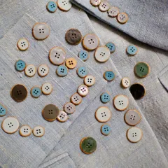 The full set of 66 custom buttons scattered on the fabric they were designed for. Each one was handmade to match the client's specific vision.