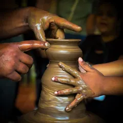 A close-up view of hands working together on the pottery wheel. This activity is a wonderful way for parents and children to connect and create a shared memory.