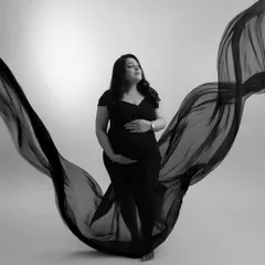 A classic black and white portrait. The flowing fabric creates a beautiful, wing-like silhouette, highlighting the mother's form with artistic and timeless elegance.