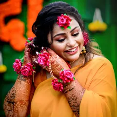 A close-up of the bride, smiling as she adjusts her floral jewelry. We capture the intricate details of your Haldi look, from the floral accessories to the henna.
