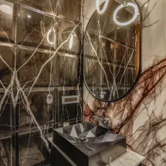 A dramatic powder room featuring a mix of two bold marbles and a wall of beveled, dark-mirrored tiles. A geometric-faceted sink and a modern, ring-lit mirror complete this high-impact design.