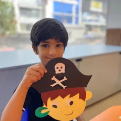 This young pirate is ready for an adventure! He's showing off the pirate mask he created, a craft that ties directly into our storytelling and role-play themes.