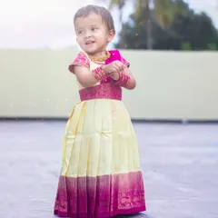 A full-length view of the cream and pink Pattu Pavadai. The pleated skirt allows for easy movement, and the silk fabric with its wide zari border gives it a classic, festive look.
