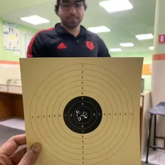 A student holding up his target, showing a very tight grouping of shots in the center. This is the result of consistent practice.